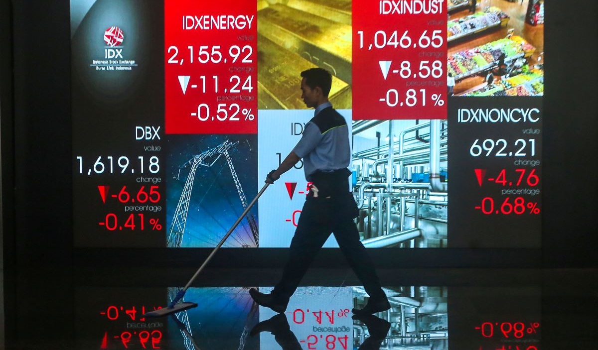 Pekerja melakukan aktivitas dengan latar belakang layar yang menampilkan pergerakan Indeks Harga Saham Gabungan (IHSG) di BEI.