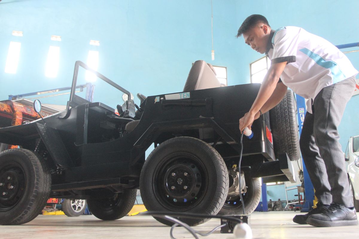 Pelajar menunjukkan cara pengisian ulang baterai mobil listrik.