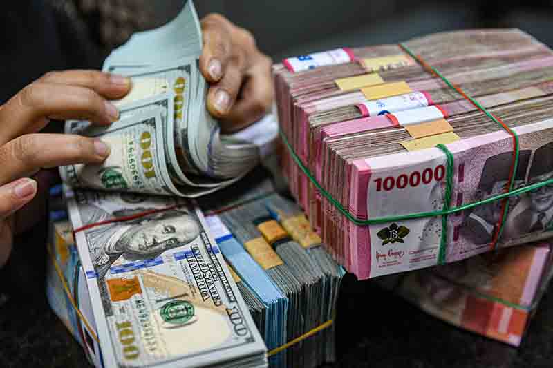 Petugas menghitung uang pecahan dolar AS dan rupiah. 