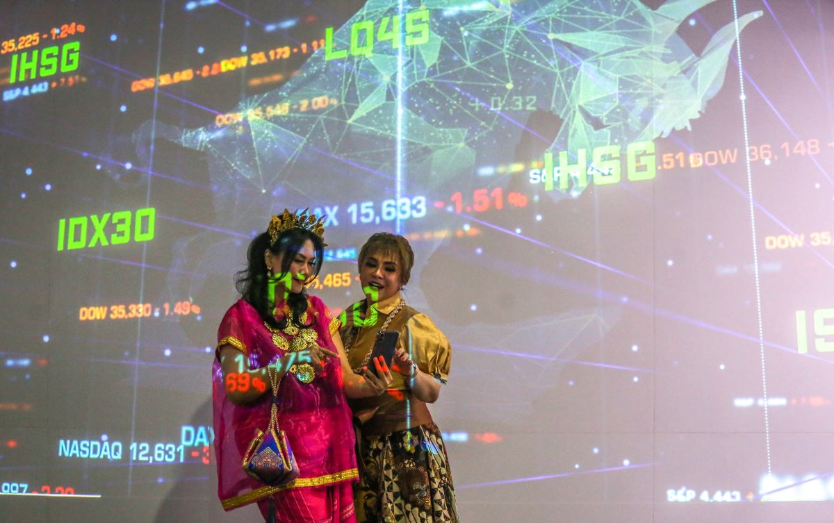 Pengunjung berfoto dengan latar belakang layar yang menampilkan pergerakan Indeks Harga Saham Gabungan (IHSG) di Bursa Efek Indonesia.