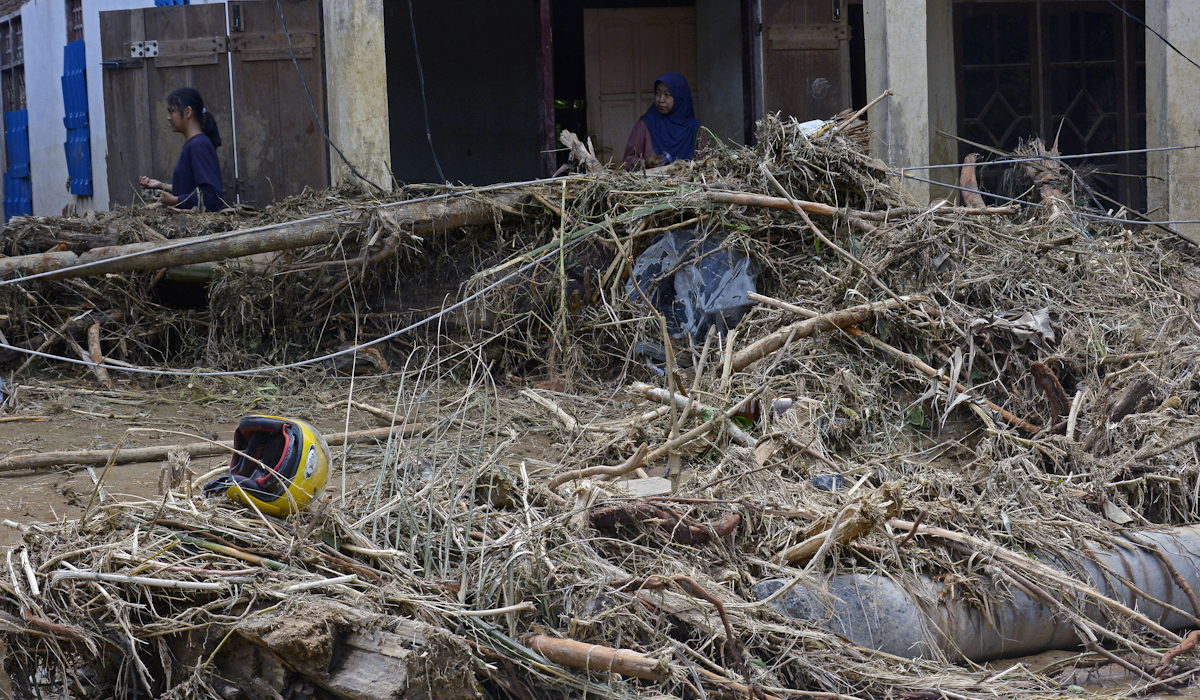 Warga melintas di depan rumah yang terdampak banjir bandang di Desa Kaili, Kecamatan Suli Barat, Kabupaten Luwu, Sulawesi Selatan