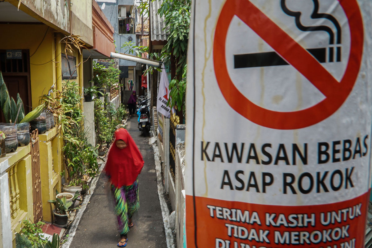 Warga berjalan dengan latar depan poster informasi kawasan bebas asap rokok di permukiman padat penduduk di Kayu Manis, Matraman, Jakarta.