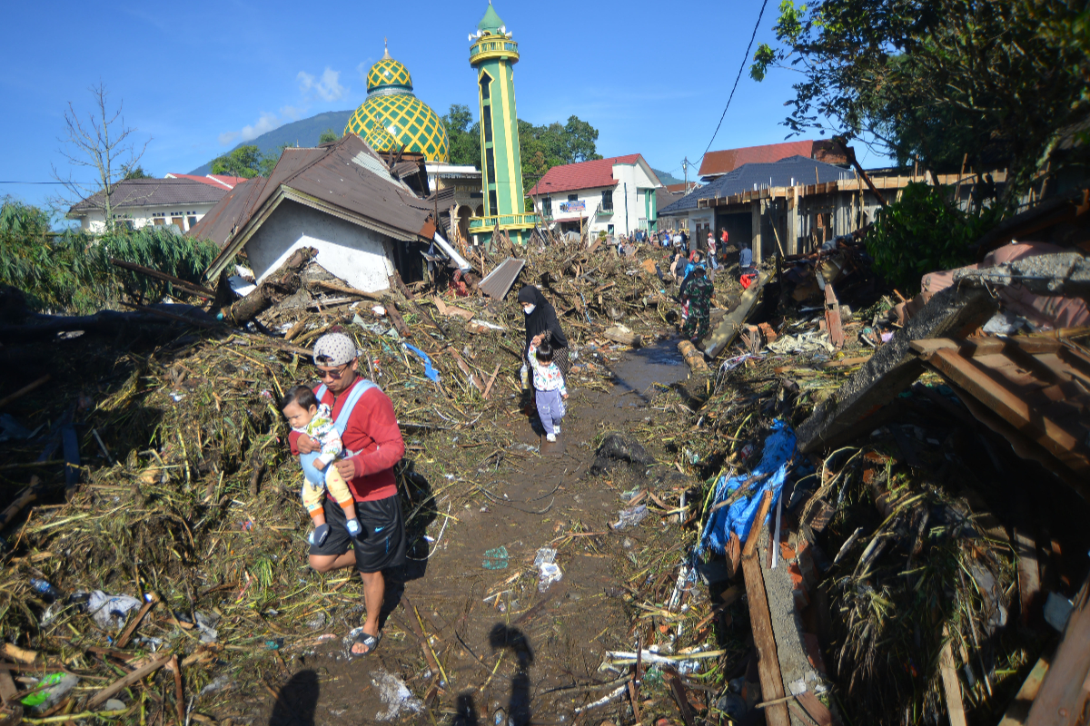 Warga berjalan di atas tumpukan material akibat banjir bandang di Jorong Galuang, Nagari Sungai Pua, Agam, Sumatera Barat, Senin (13/5/2024)
