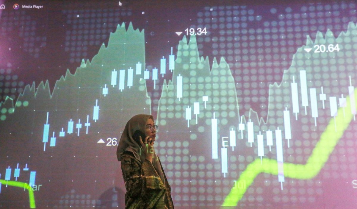 Seorang pialang melakukan aktivitas dengan latar belakang layar yang menampilkan pergerakan Indeks Harga Saham Gabungan (IHSG) di BEI.