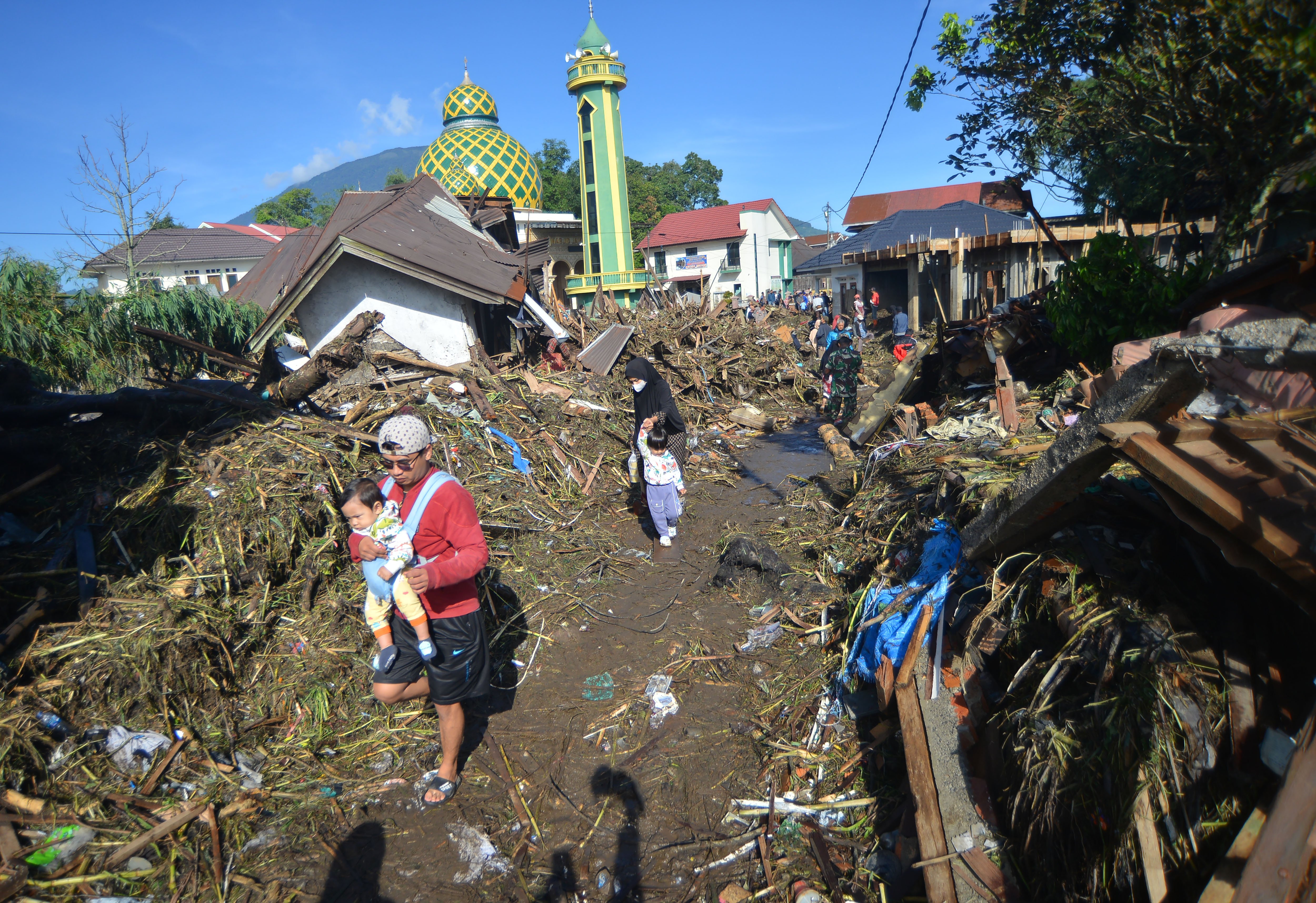 Warga berjalan di atas tumpukan material akibat banjir bandang di Jorong Galuang, Nagari Sungai Pua, Agam, Sumatera Barat, Senin (13/5/2024)