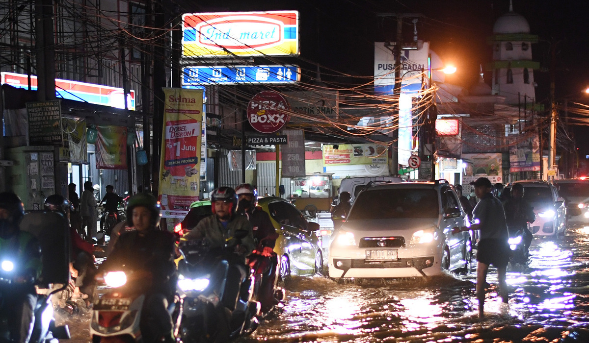 Pengendara melintasi Jalan Sawangan yang tergenang akibat luapan Kali Licin di Mampang, Depok.