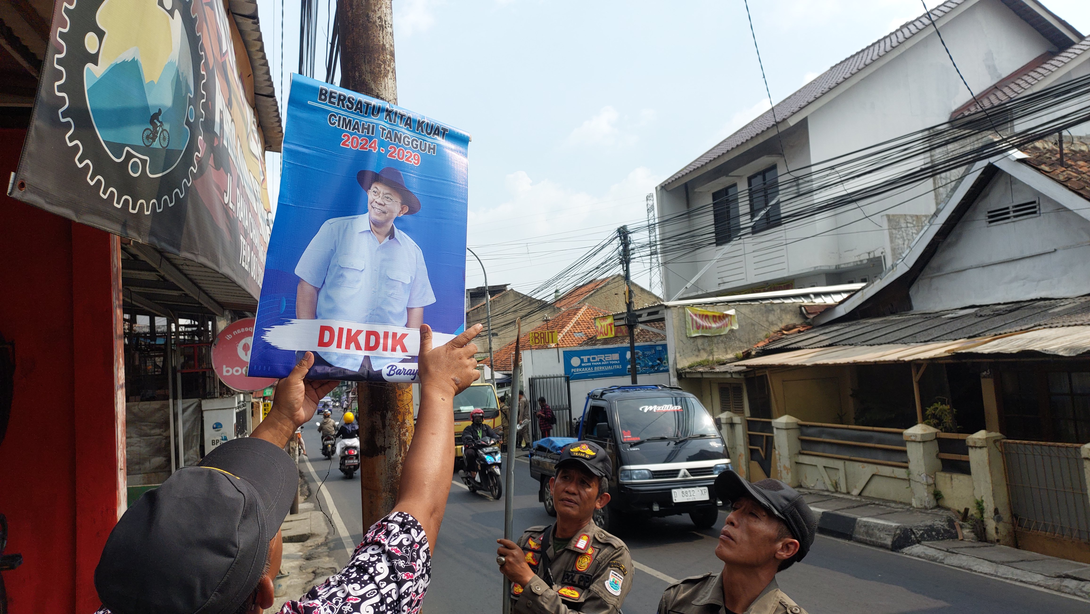 Anggota Satpol PP Kota Cimahi menurunkan alat peraga kampanye bergambar Sekda Kota Cimahi Dikdik S Nugrahawan 