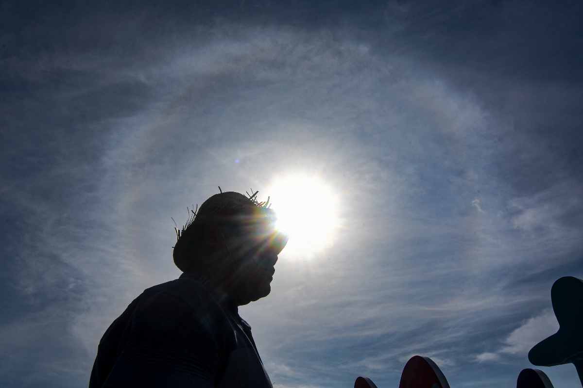 Seorang laki-laki berdiri di areal tugu Mataram Metro dengan latar belakang Halo Matahari di Mataram, NTB, Selasa (19/7/2022). Halo matahari