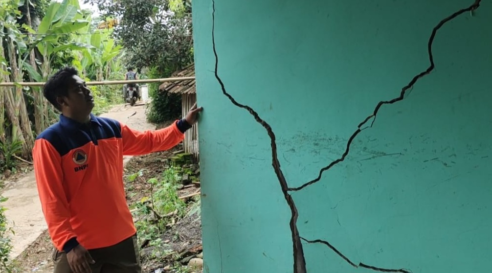 Seorang petugas menunjukkan tembok rumah yang rusak akibat pergerakan tanah di Cianjur.