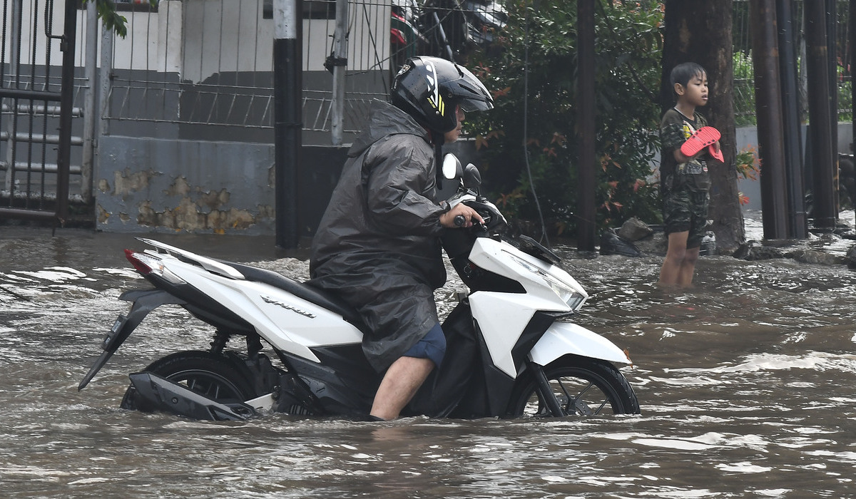 Pengendara sepeda motor mendorong motornya yang mogok terendam banjir di Bekasi.