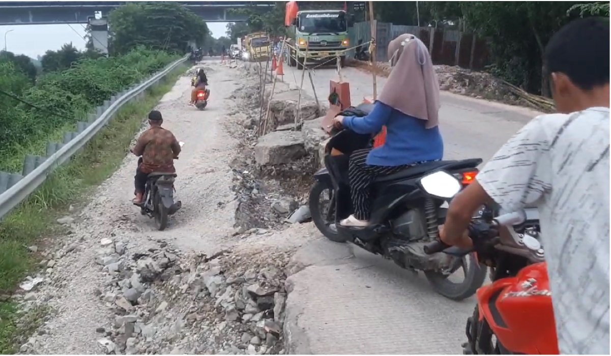Warga melewati jalan ambles di Karawang.