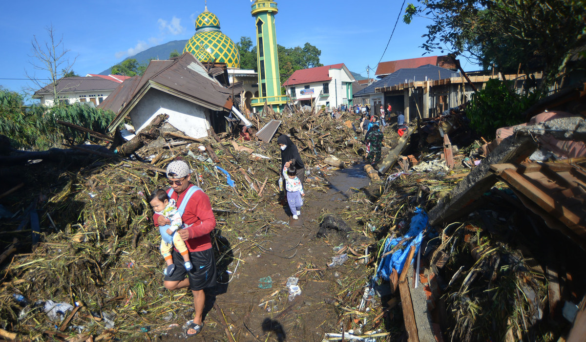 Warga berjalan di atas tumpukan material akibat banjir bandang di Agam, Sumbar.
