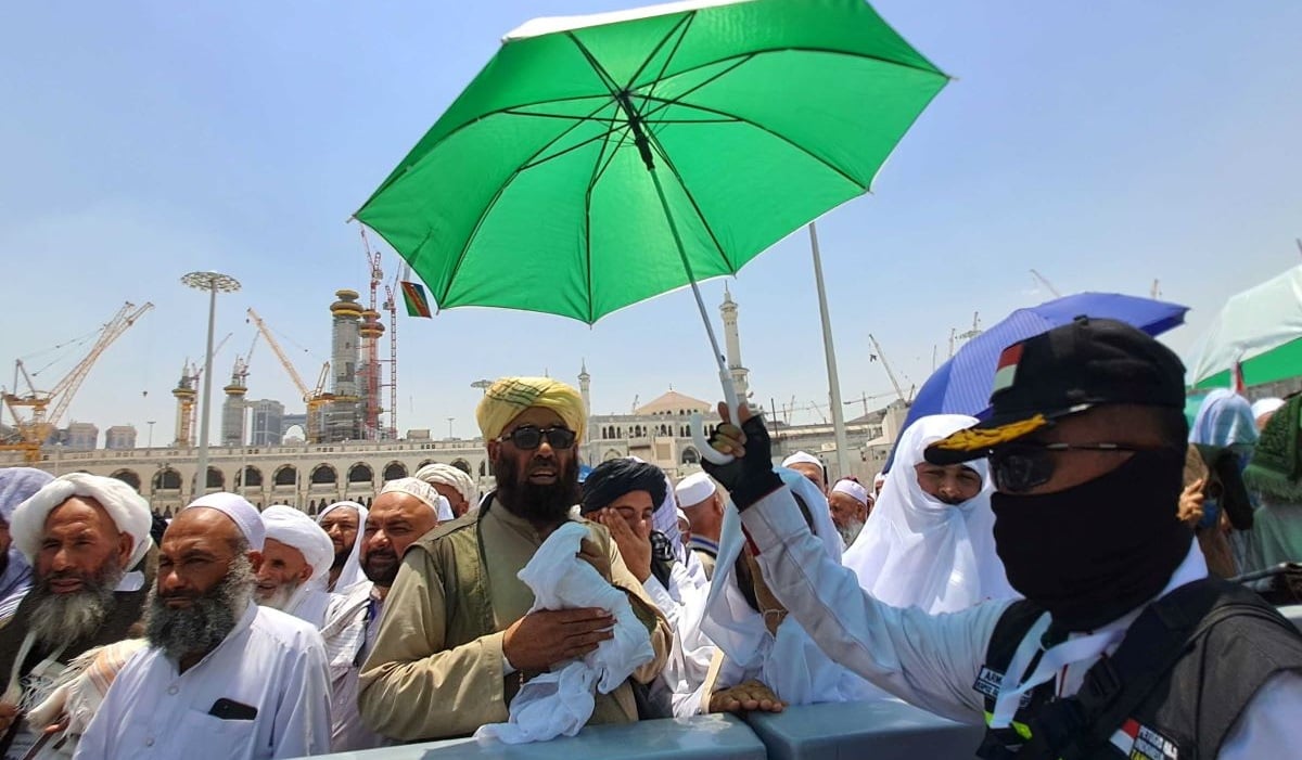 Seorang petugas PPIH Arab Saudi memayungi jamaah saat menunggu dibukanya jalan menuju terminal Bir Ali di Mekah, Arab Saudi.