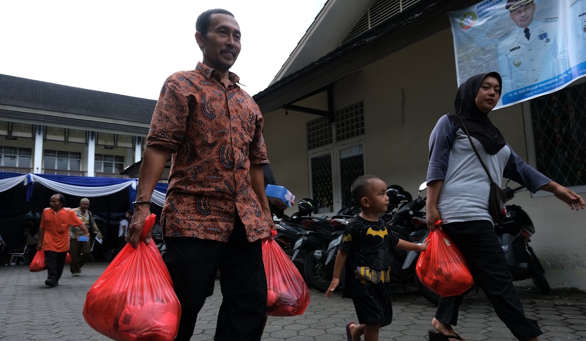 Sejumlah warga membawa paket sembako usai menerima pembagian penyaluran bahan pangan DTKS Non Bansos