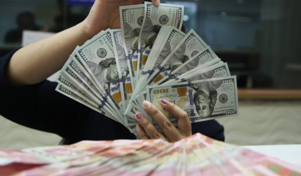 Petugas menunjukkan uang pecahan dolar dan rupiah di gerai penukaran mata uang asing di Jakarta.