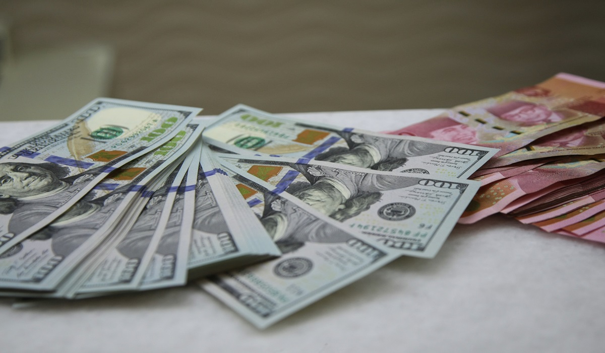 Petugas menunjukkan uang pecahan dolar dan rupiah di gerai penukaran mata uang asing di Jakarta, Selasa (18/06/2024).