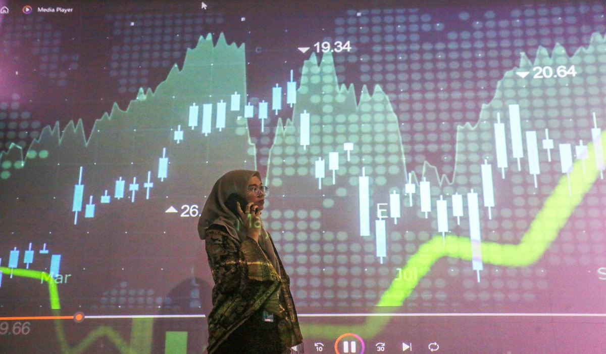 Seorang pialang melakukan aktivitas dengan latar belakang layar yang menampilkan pergerakan IHSG di Bursa Efek Indonesia, Jakarta.