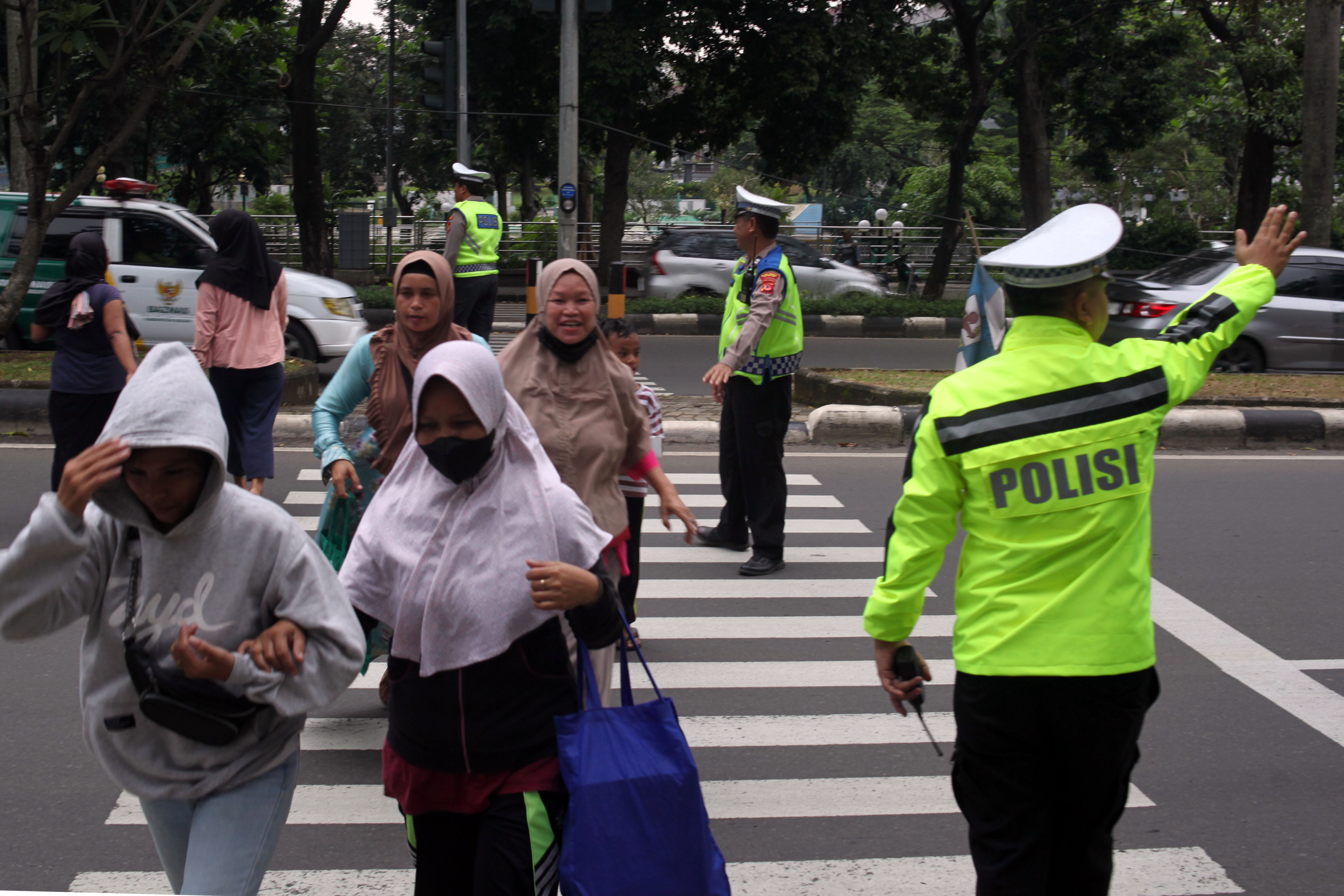 Personel Satlantas Polres Bogor membantu warga menyebrang di Jalan Raya Tegar Beriman, Kabupaten Bogor, Jawa Barat. 