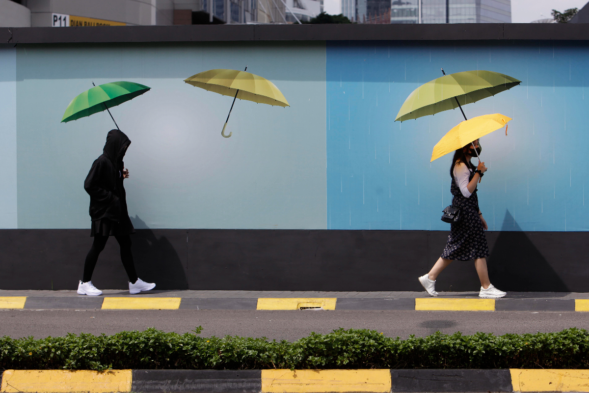 Pejalan kaki berlindung dari sengatan matahari menggunakan payung saat melintasi kawasan Karet. Jakarta