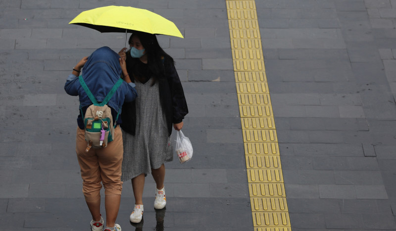 Pekerja menggunakan payung menghiindari guyuran hujan