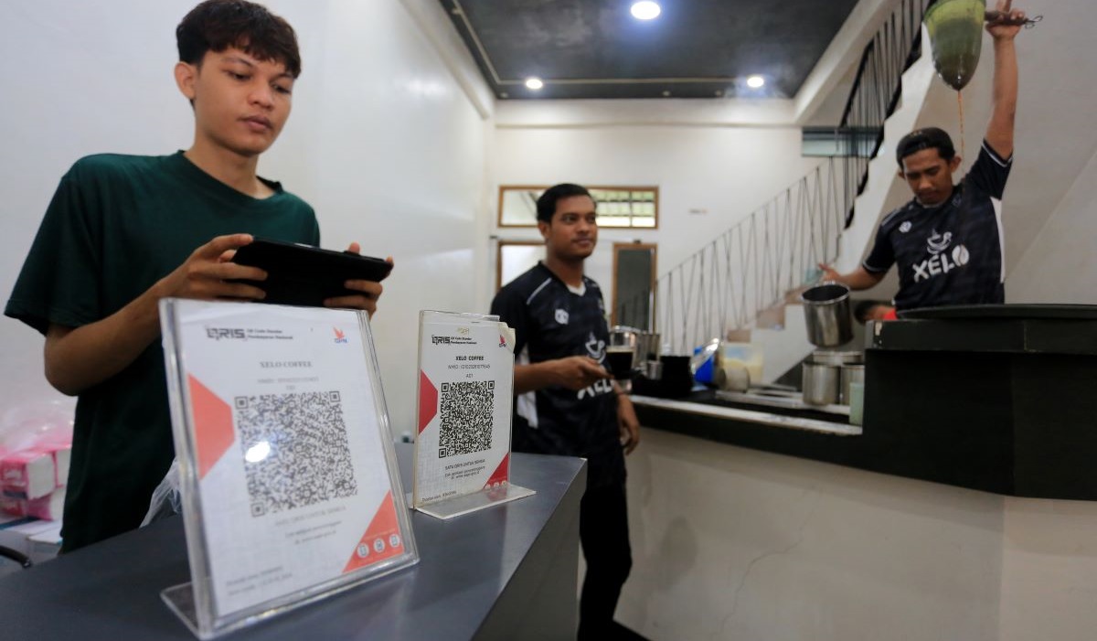 Pelayan membawa kopi pesanan pelanggan di salah satu warung kopi yang menyediakan QRIS di Meulaboh, Aceh.
