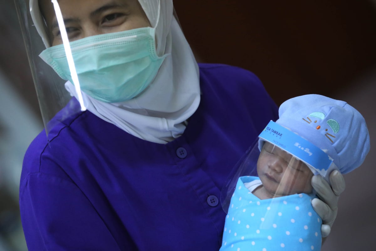 Perawat tersenyum saat menunjukkan bayi yang memakai pelindung muka atau 'face shield' untuk bayi di RS Ibu dan Anak Tambak