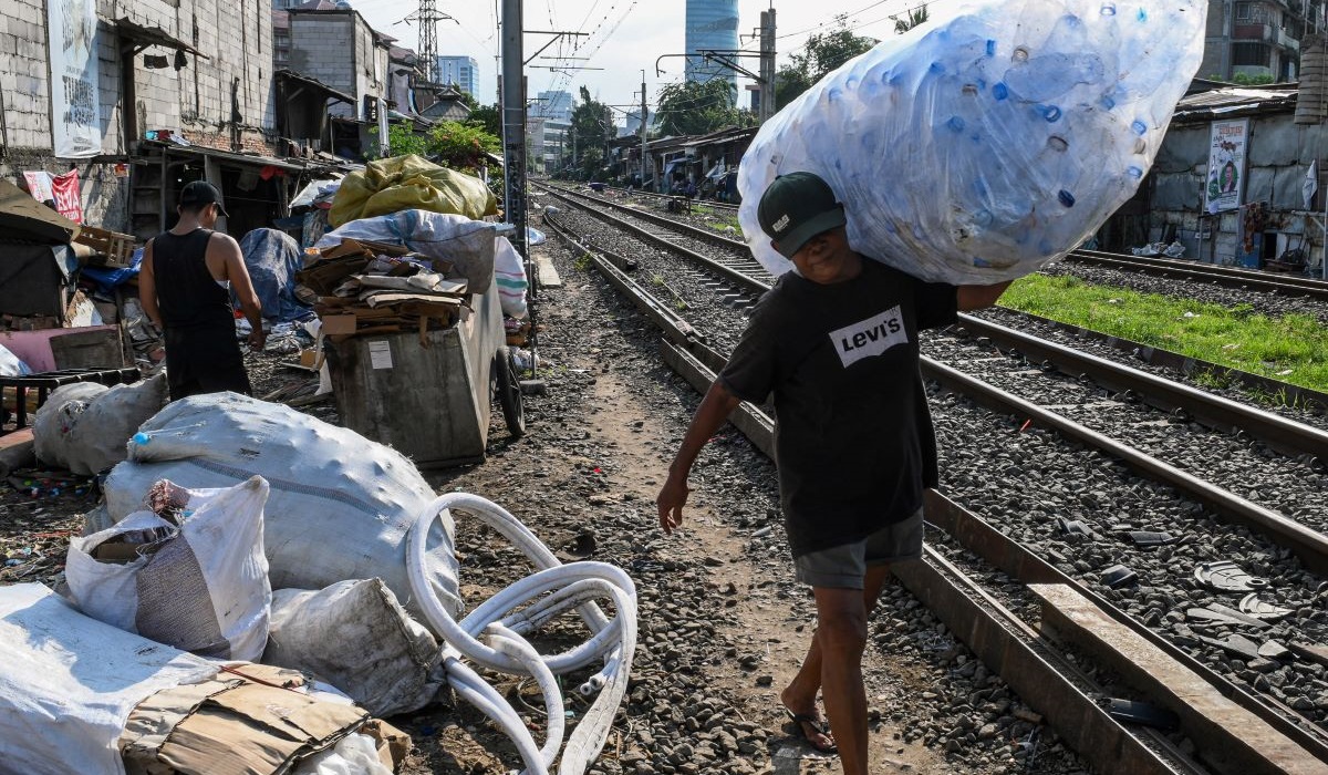 Pemulung memikul botol plastik di area perlintasan kereta api Palmerah-Tanah Abang, Jakarta, Jumat (5/1/2024).