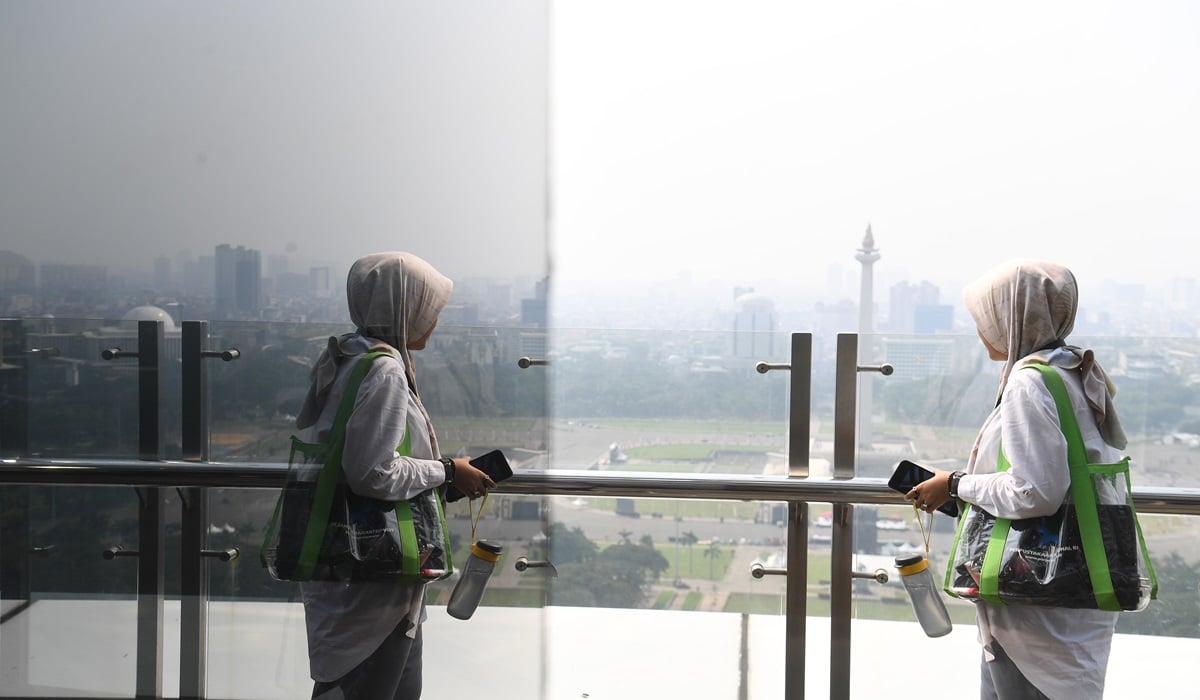 Seorang perempyan melintas dengan latar belakang Monas yang tertutup polusi di Jakarta.