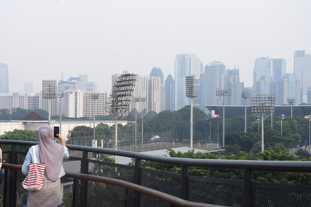 Warga berfoto dengan latar belakang gedung-gedung bertingkat yang diselimuti kabut di Skywalk Senayan Park, Jakarta, Rabu (30/3/2022).