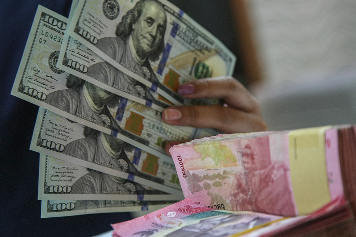 Petugas menunjukkan uang pecahan dolar dan rupiah di gerai penukaran mata uang asing di Jakarta, Selasa (18/06).