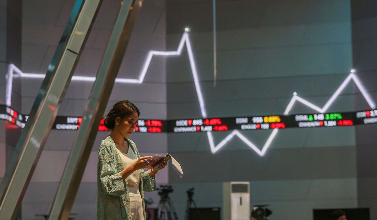  Seorang pialang melakukan aktivitas dengan latar belakang layar yang menampilkan pergerakan IHSG di Bursa Efek Indonesia.