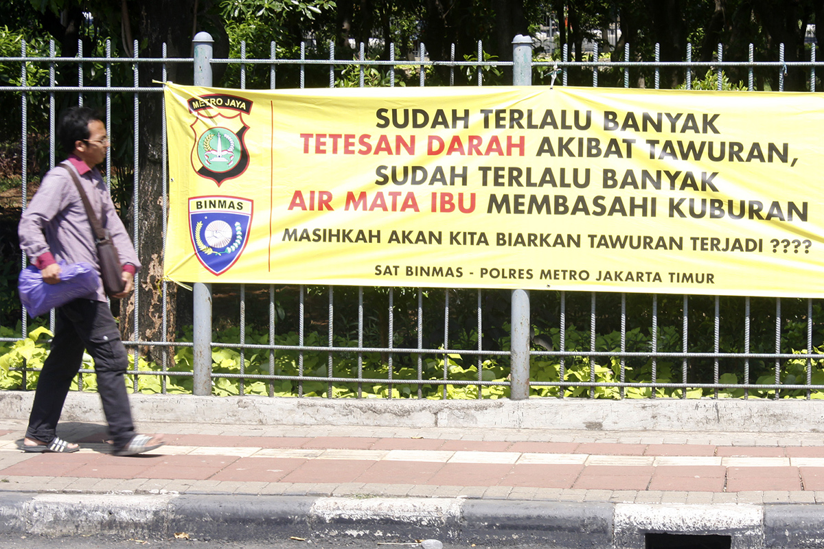 Warga melintasi spanduk bertuliskan pesan dampak negatif dari tawuran.