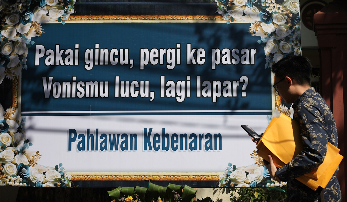 Warga berjalan di dekat karangan bunga yang terpajang di depan Gedung Pengadilan Negeri Surabaya 