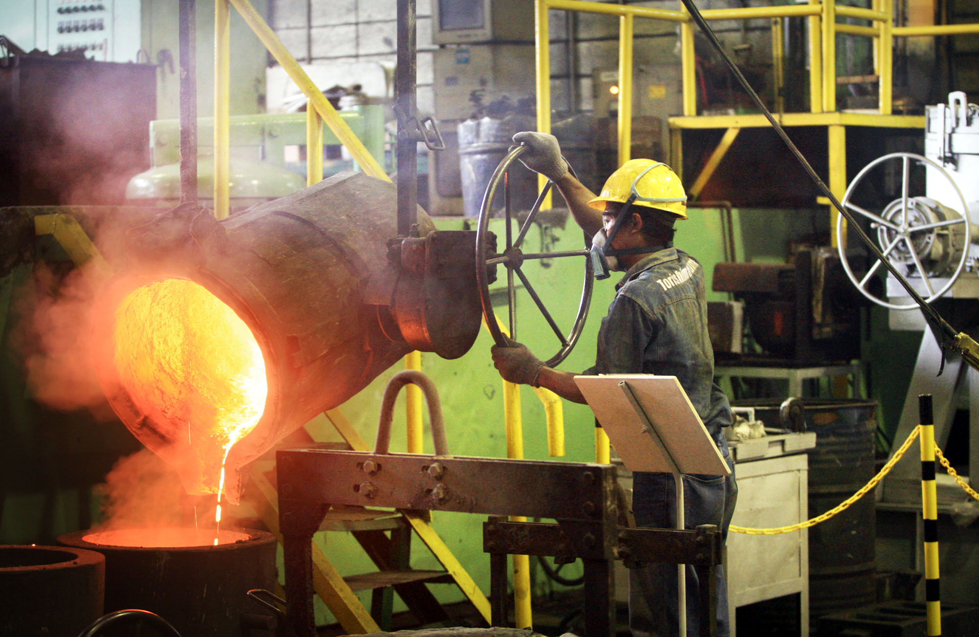 Pekerja tengah menuangkan cor baja untuk cetakan.