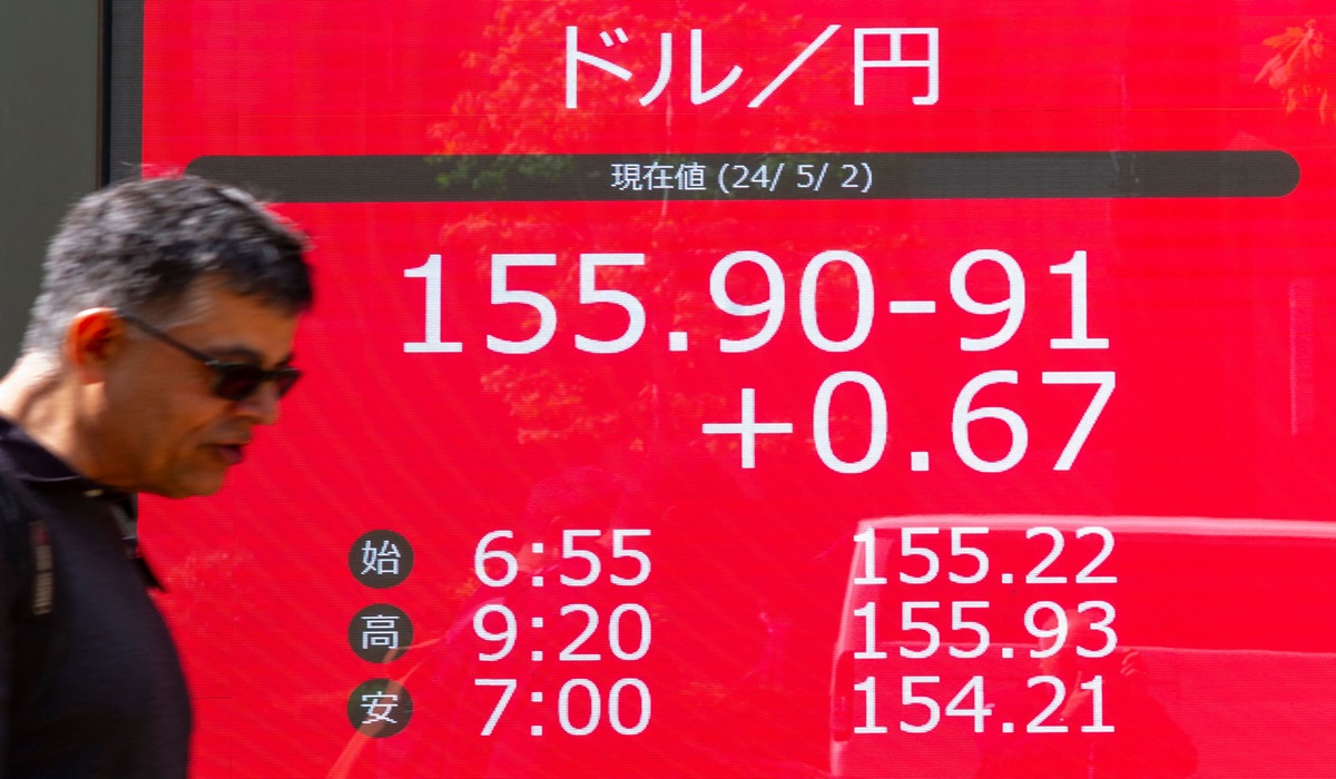Seorang warga berjalan di depan layar yang menampilkan nilai mata uang yen terhadap dolar AS di Tokyo, Jepang.