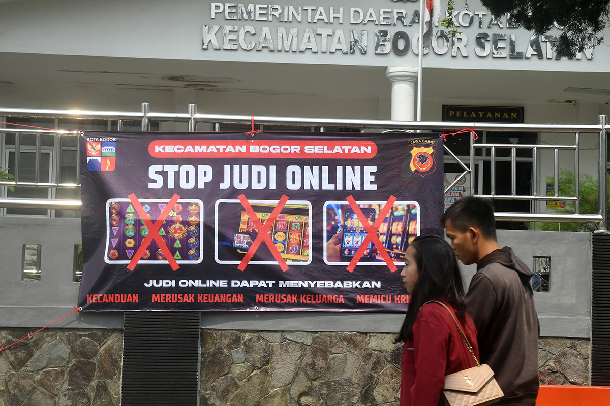 Warga berjalan di depan spanduk sosialisasi larangan judi online di Kantor Kecamatan Bogor Selatan, Kota Bogor, Jawa Barat, Senin (1/7).
