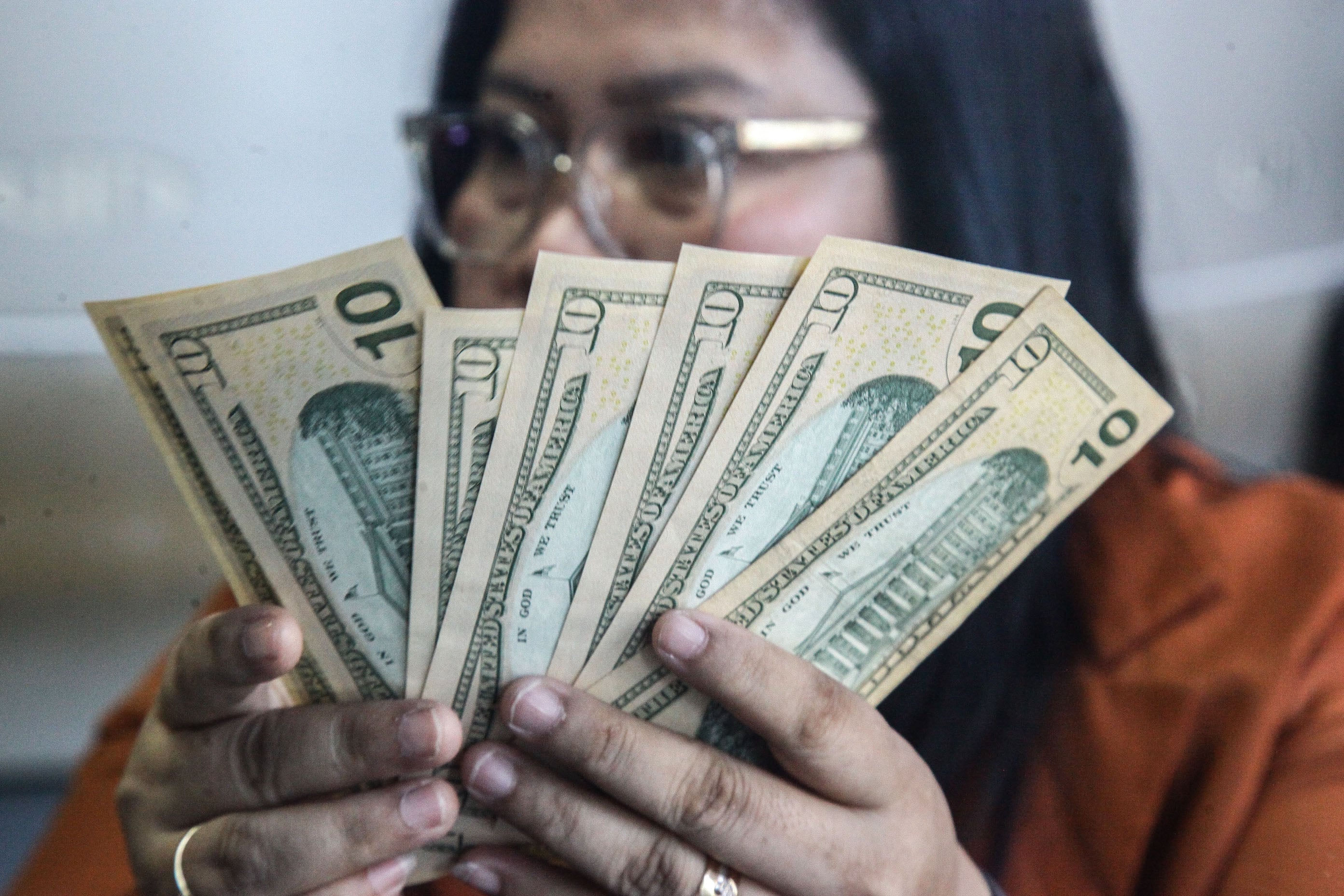 Petugas menghitung uang pecahan dolar AS dan rupiah di gerai jasa penukaran mata uang asing.