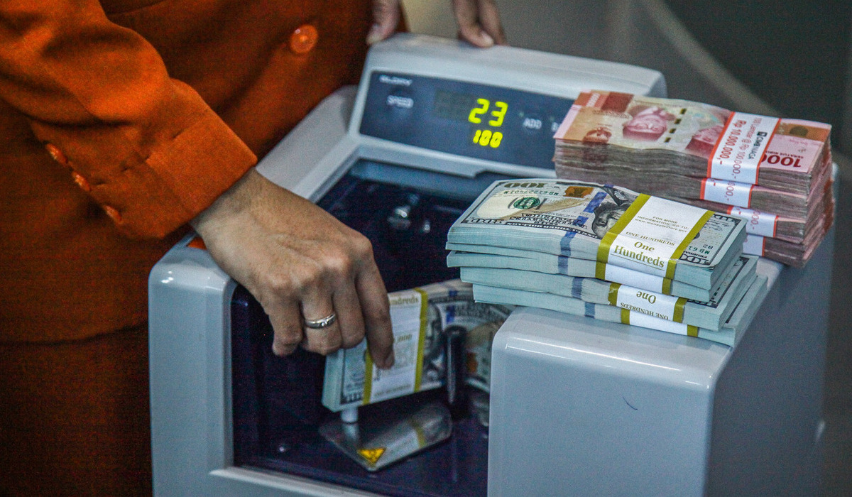 Petugas menghitung uang pecahan dolar AS dan rupiah di gerai jasa penukaran mata uang asing.