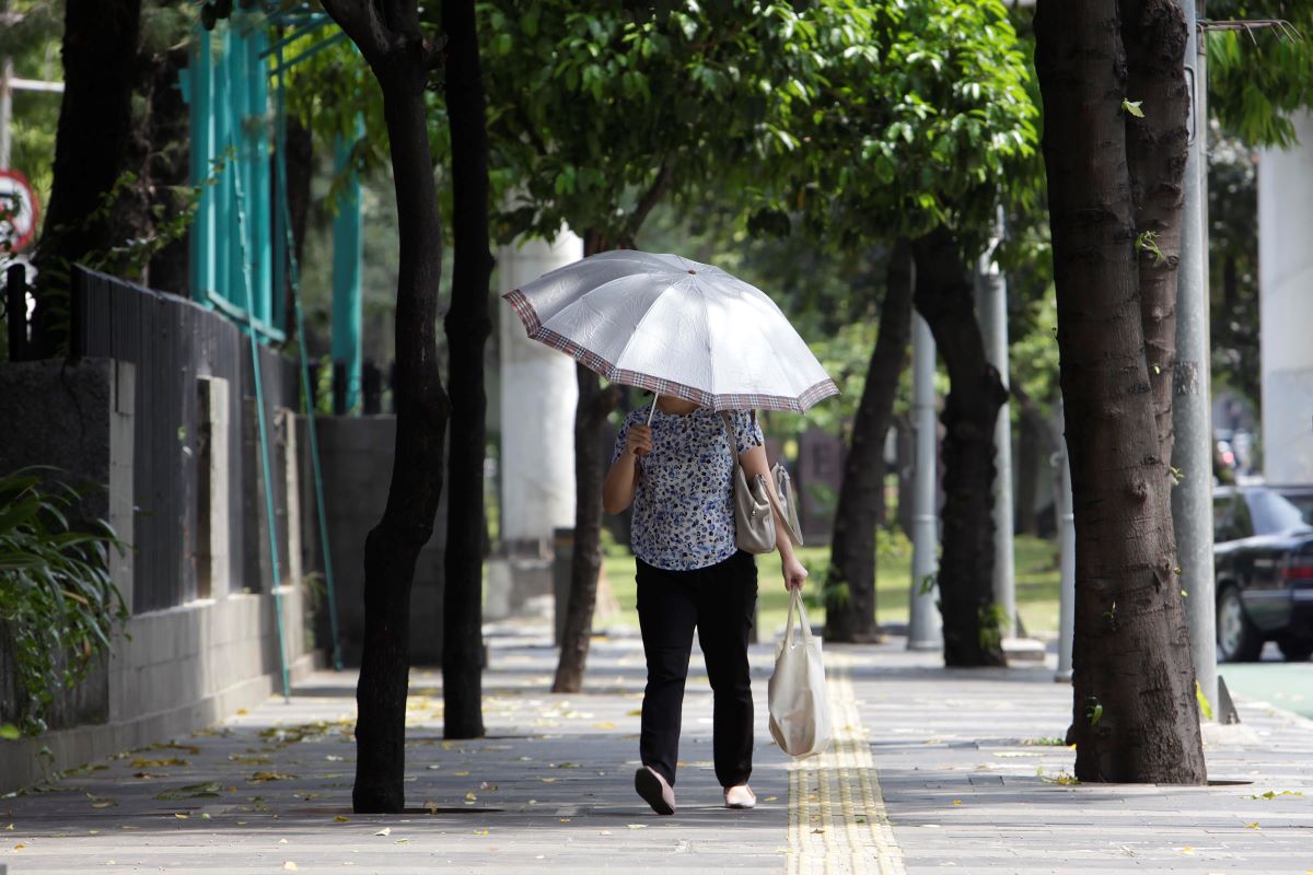 Pejalan kaki berlindung dari sengatan matahari saat melintasi pedestrian kawasan Sudirman, Jakarta.