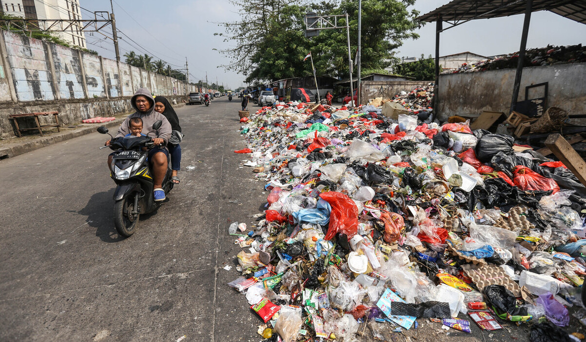 Warga melintas di samping sampah di Tempat Pembuangan Sampah Sementara (TPSS), Pancoran Mas, Depok.